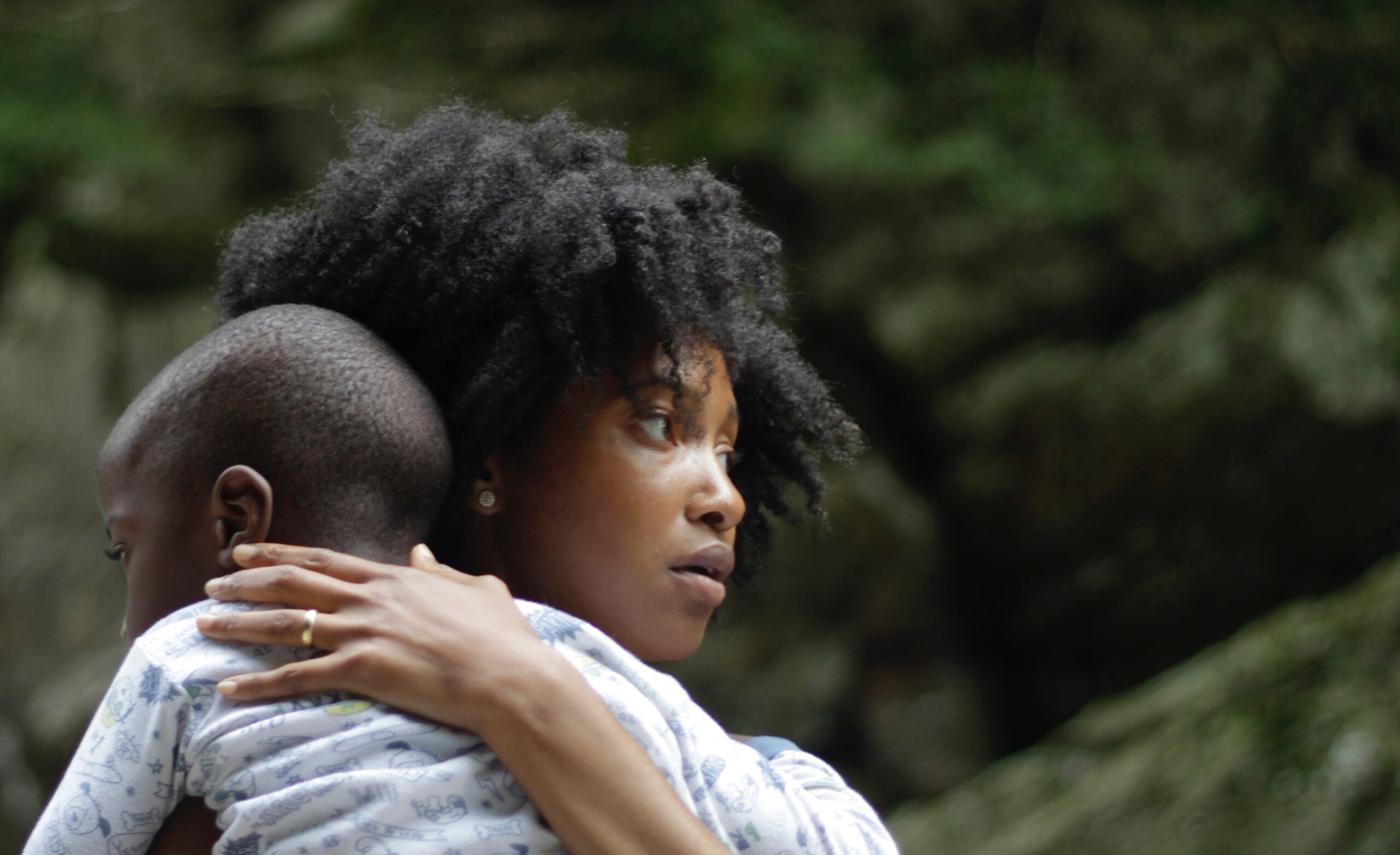 a woman holding a small child in the foreground with forest in the background