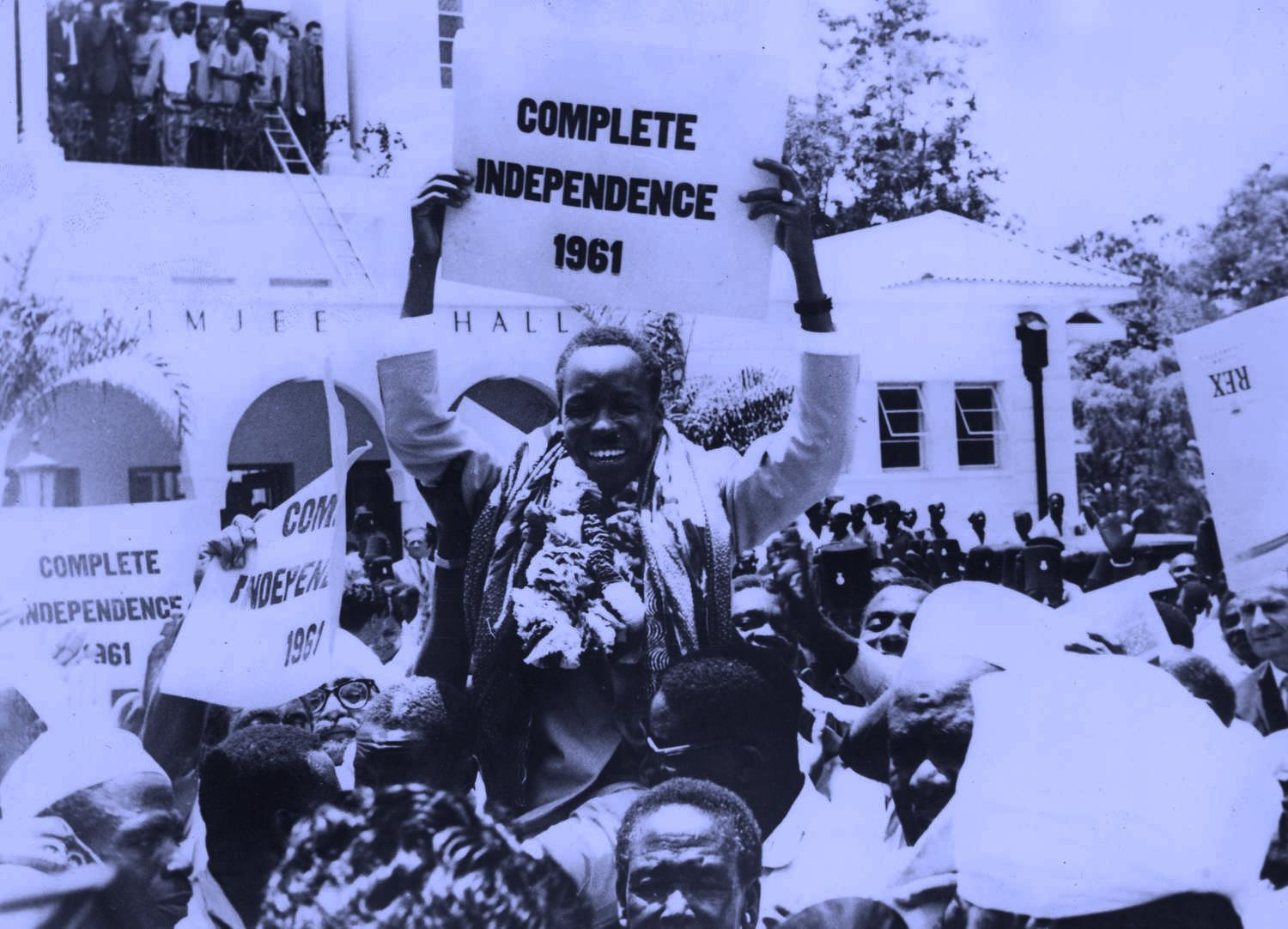 black and white photo of a crowd, one man sits on another mans shoulders, smiling and holding a sign that reads Complete Independence 1961